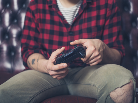 A young man is sitting on a sofa and is playing video gamesの写真素材