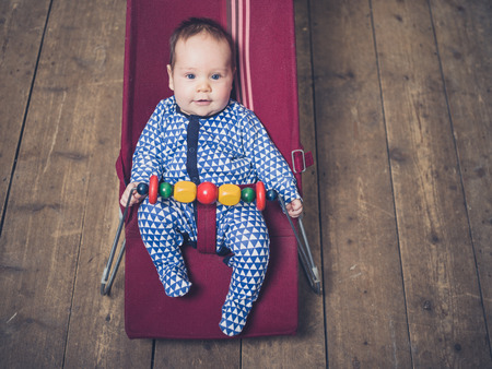 A baby is sitting in a vintage bouncy chair on the wooden floorの写真素材