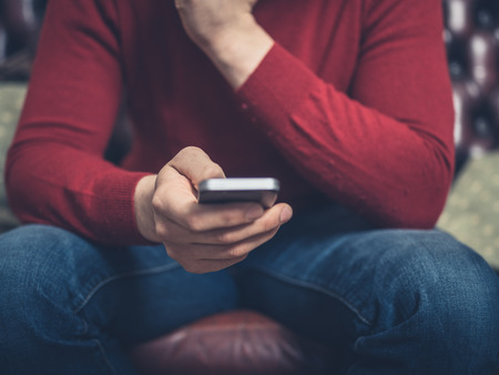Close up on a man sitting on a sofa using a smartphoneの写真素材