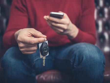 Close up on a man sitting on sofa with a smartphone and car keysの写真素材