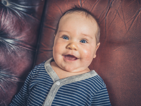 A small baby is lying on a leather sofa with a happy smile on his faceの写真素材