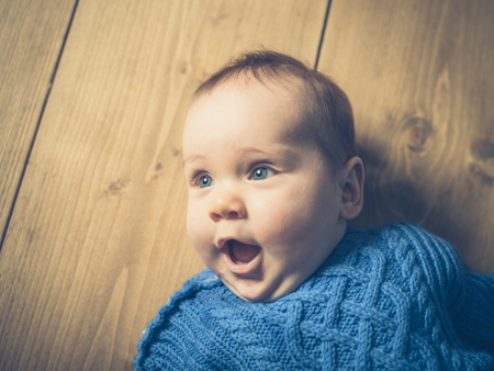 A happy and surprised baby lying on a wooden floorの写真素材