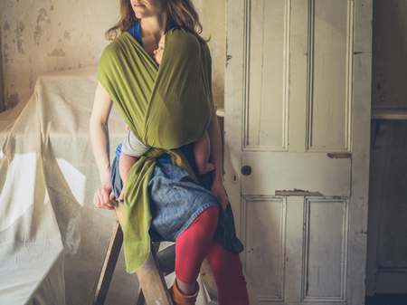 A young mother is sitting on a ladder with her baby in a room being decoratedの写真素材