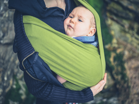 A young mother is standing outside in nature with her baby in a slingの写真素材