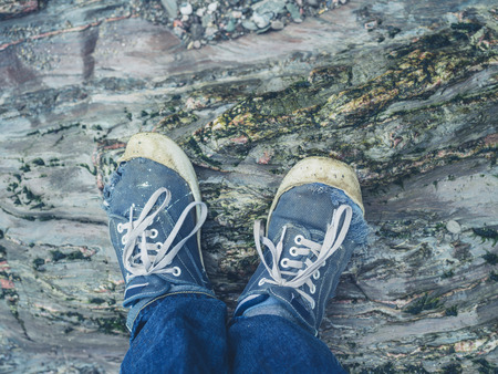 The feet of a young man wearing trainers standing on the rocksの写真素材