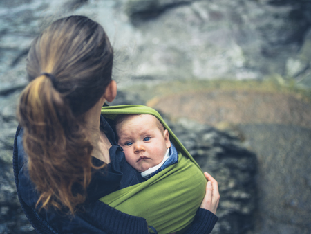 A young mother is standing outside in nature with her baby in a slingの写真素材