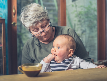 A grandmother is sitting at a dining table with her baby grandchildの写真素材
