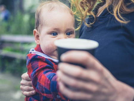 A little baby is grabbing the paper cup his mother is holding outsideの写真素材