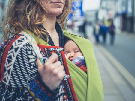 A young mother in the street with her baby in a carrier slingの写真素材