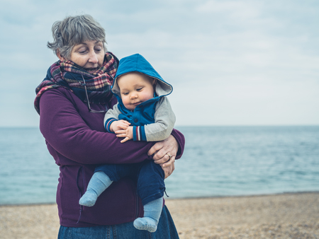 A grandmother is on the beach holding a baby on a cold dayの写真素材