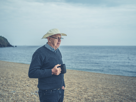 A senior man is standing on the beach with a cup of drink in his handの写真素材