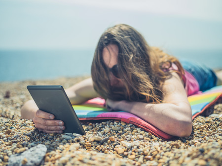 A young woman is on the beach and is reading from a digital tabletの写真素材
