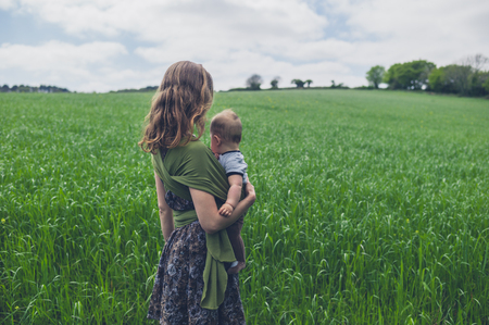 A young mother is standing in a field of grass with her babyの写真素材