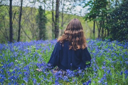 A young woman is sitting in a meadow of bluebellsの写真素材