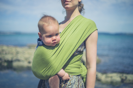 A young mother is walking on the coast with her baby in a slingの写真素材
