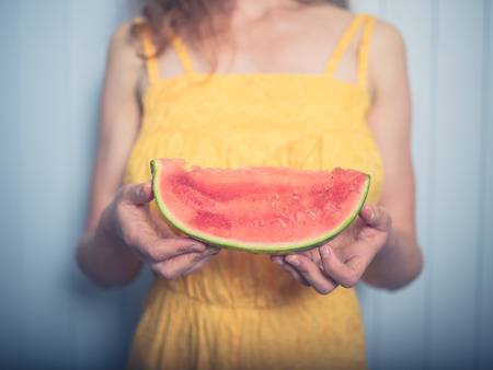 A young woman in a yellow dress is eating water melonの写真素材
