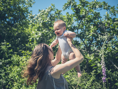 A young mother is lifting her baby up in the air outside in natureの写真素材