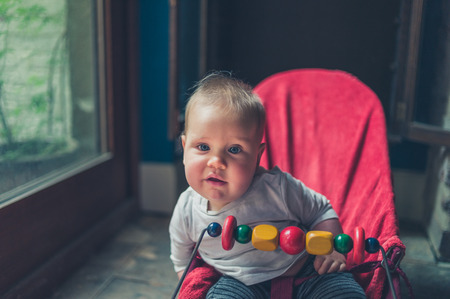 A little baby is sitting in a bouncy chair by the windowの写真素材