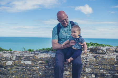 A grandfather is playing with his grandchild on a wall by the sea