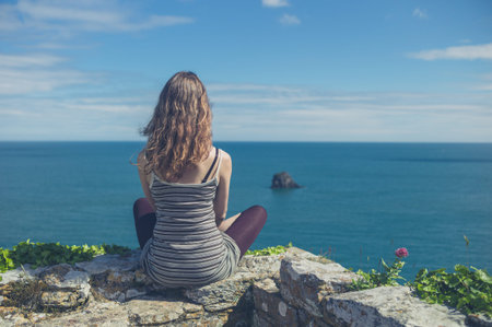 A young woman is relaxing on a wall by the sea on a summer day