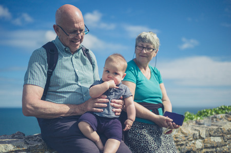 An elderly couple is sitting on a wall by the sea with their grandchildの写真素材