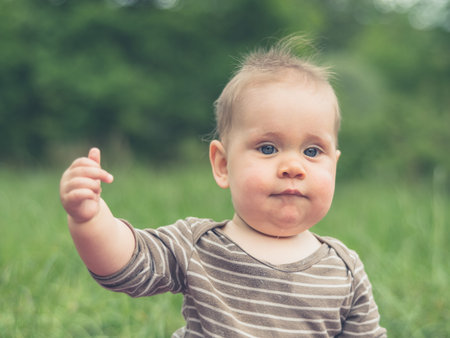 A cute little baby is sitting in nature and is making a gesture with his middle finger