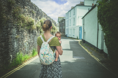 A young mother with her baby in a sling is walking in a villageの写真素材