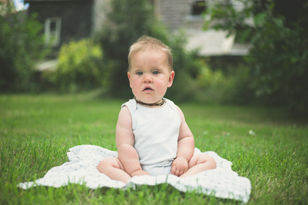A cute little baby is sitting on the grass outside in the parkの写真素材