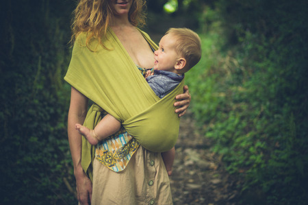 A young mother with her baby in a sling is standing in a forestの写真素材