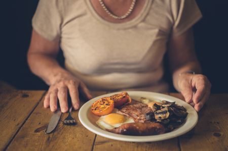 A senior woman is in a cafe eating a traditional english breakfastの写真素材