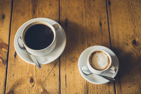 A cup of black coffee and a cup of cappucino on a wooden tableの写真素材