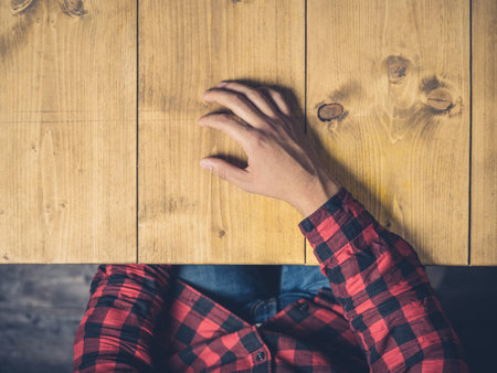 A young man is sitting at a wooden table resting his hand on itの写真素材