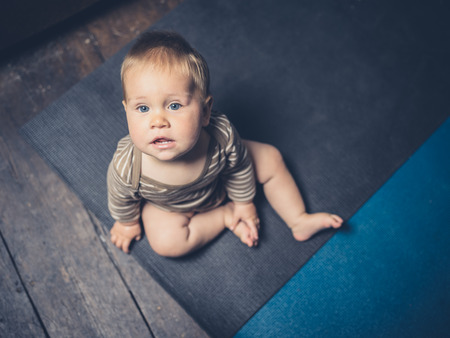 A little baby is sitting on some yoga mats on the floorの写真素材