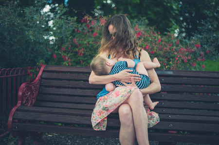 A young mother is breastfeeding her baby on a park benchの写真素材