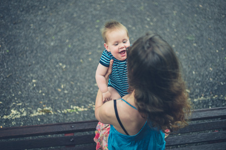 Young mother sitting on a park bench with her laughing babyの写真素材