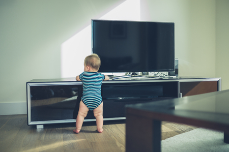 A little baby is cruising on the furniture by the televisionの写真素材