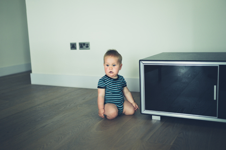 A confused little baby is sitting by the furniture on the floor at homeの写真素材