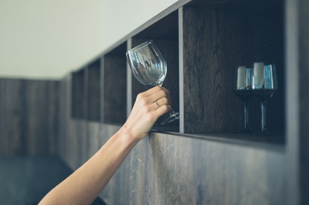 A young woman is getting a wine glass from a shelf in her kitchenの写真素材