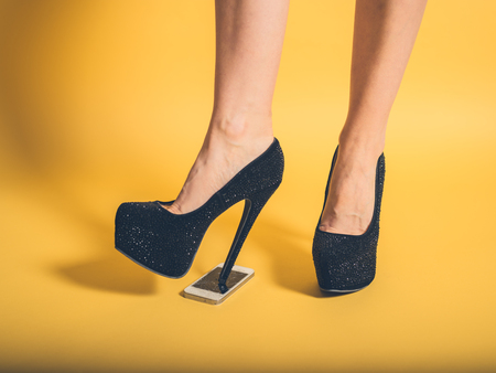 A young woman in elegant heels is stepping on a smartphoneの写真素材