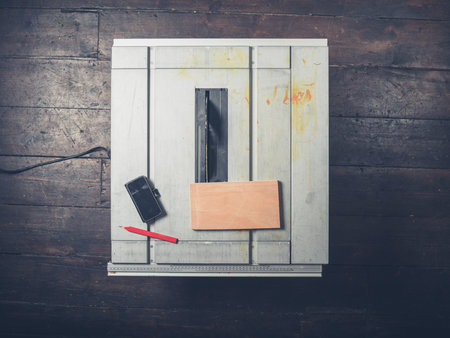 A piece of wood a pencil and a smartphone on a tablesaw