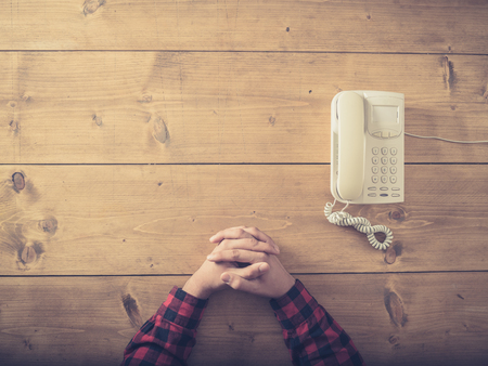 Overhead shot of a man sitting at a table with an old phone waiting for a callの写真素材