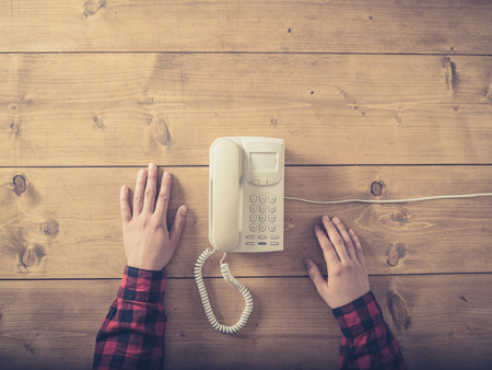 Overhead shot of a man sitting at a table with an old phone waiting for a callの写真素材
