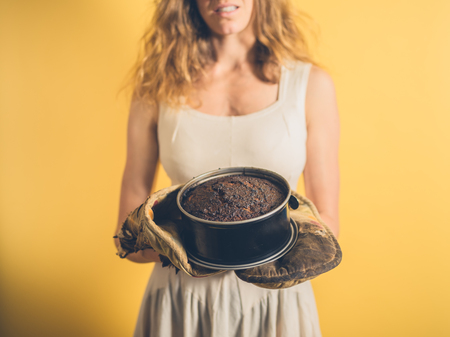 A young woman is holding a burnt cake with burnt oven glovesの写真素材