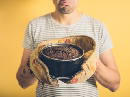 An upset young man is holding a burnt cake