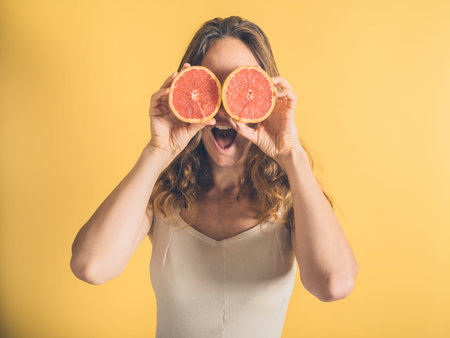 A silly young woman is pretending to use two grapefruit halves as binocularsの写真素材