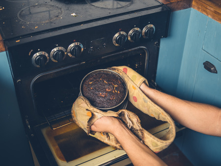 The hands of a man is removing a burnt cake from the ovenの写真素材