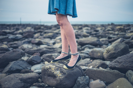 The feet and legs of a young woman wearing a skirt standing on the beach in autumnの写真素材