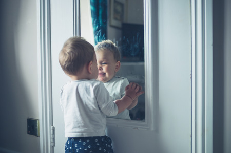 A cute little baby is playing with his own reflectionの写真素材
