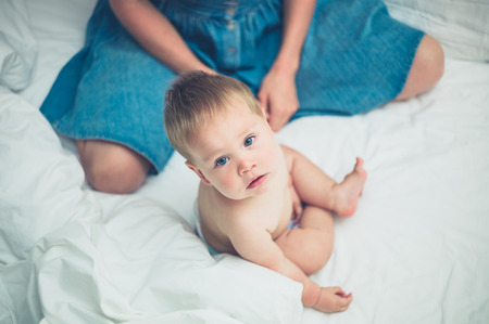 A young mother and her baby are sitting in bedの写真素材