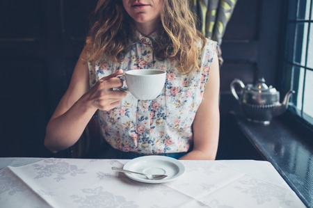 A young woman is sitting at a table by the window and is drinking coffeeの写真素材